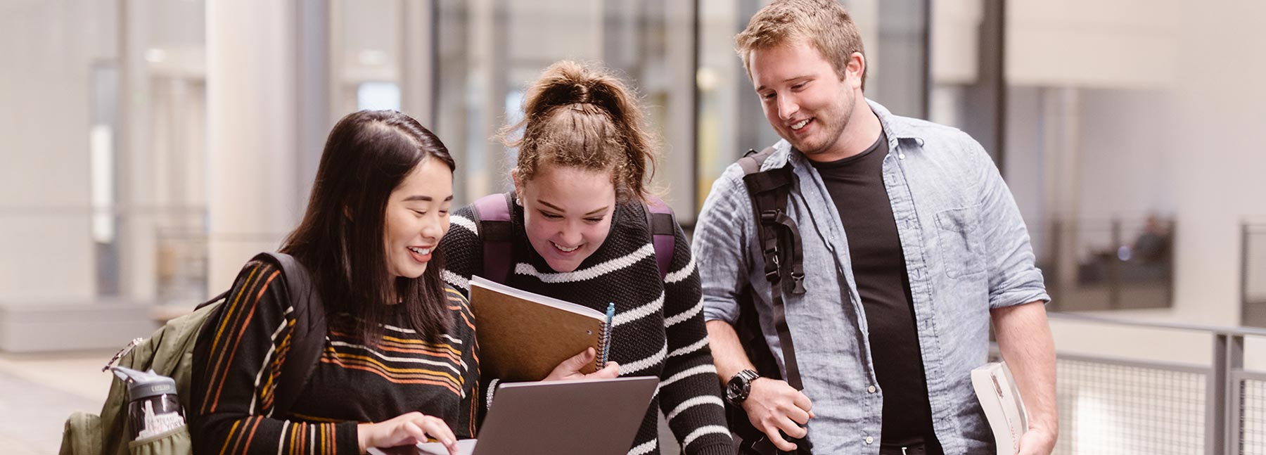 Three students look at a laptop computer together