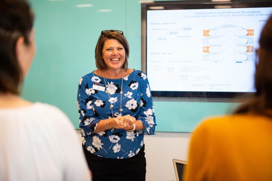 A woman stands next to a white board