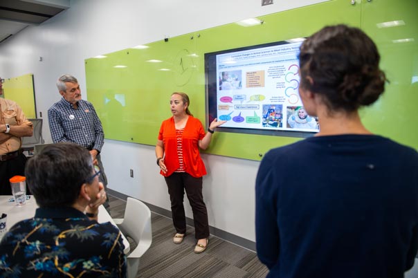 A woman points to a large monitor