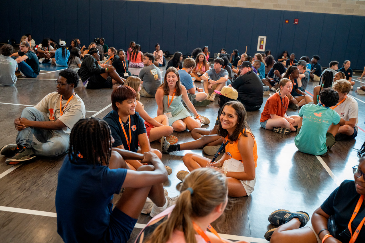 A large group of summer program participants sitting on the recreation and wellness center floor playing games, laughing, and talking.