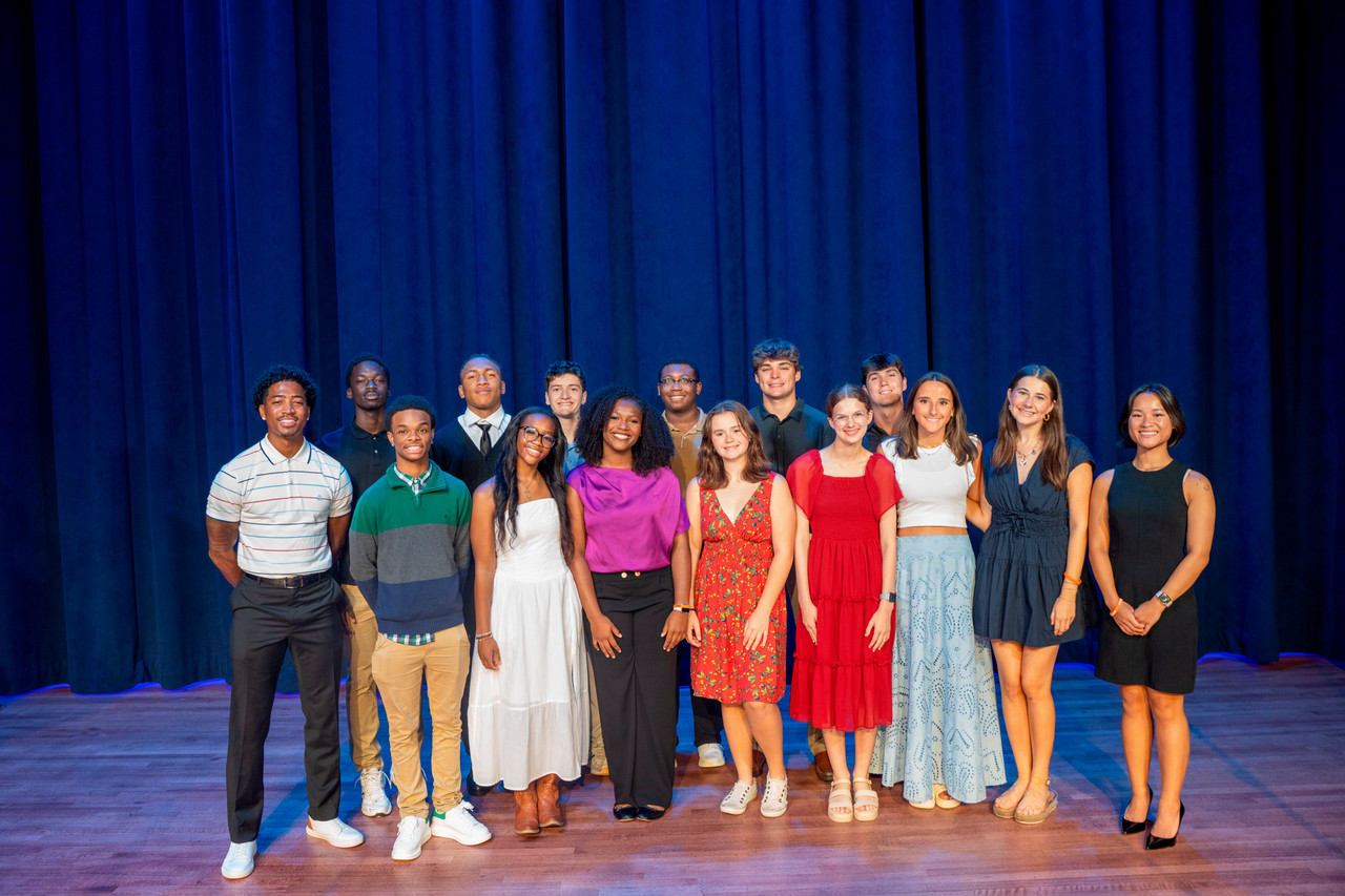 A group of summer program participants smiling on stage and posing for the camera.
