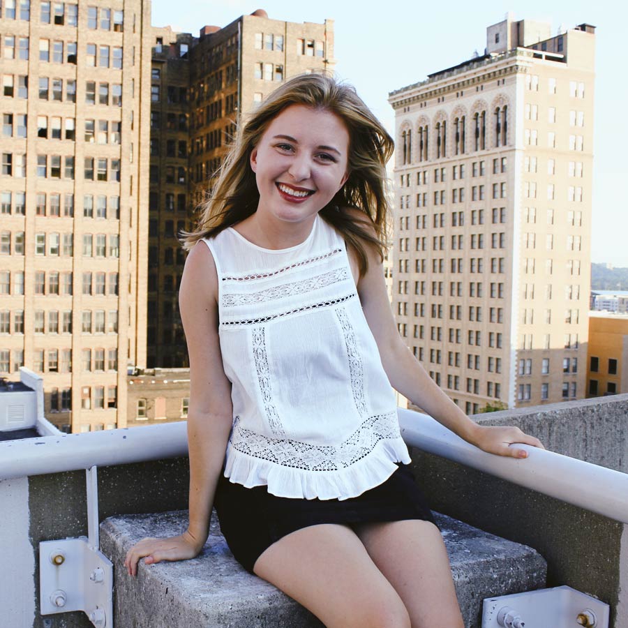 Claire in a white top sitting on top a roof with the city scape in the background.