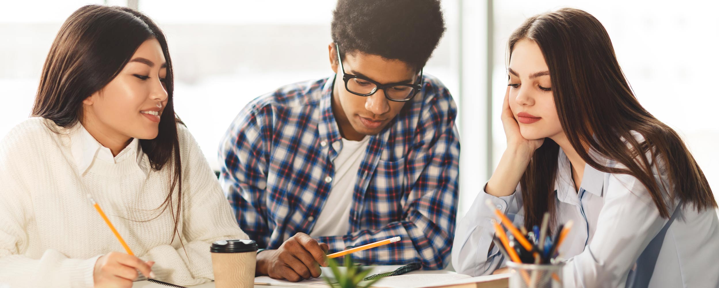 A female, male and another female student looking at notes in a notebook.