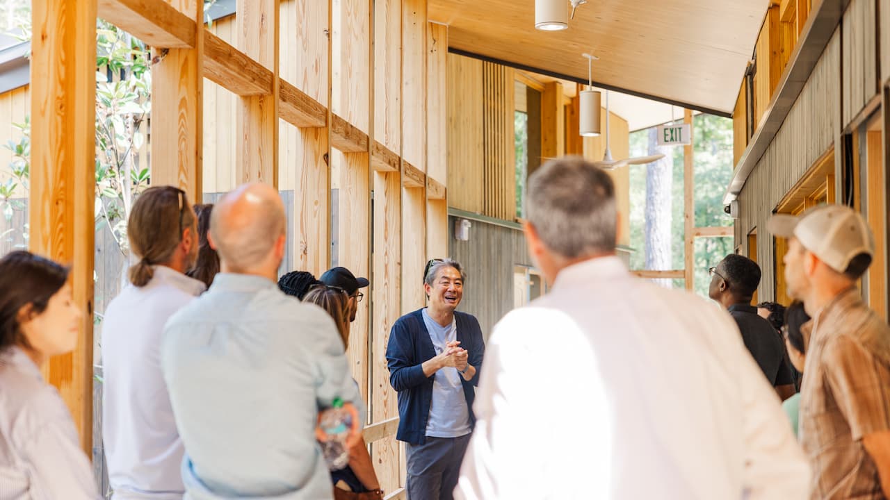 man speaking to an audience inside a wood structure