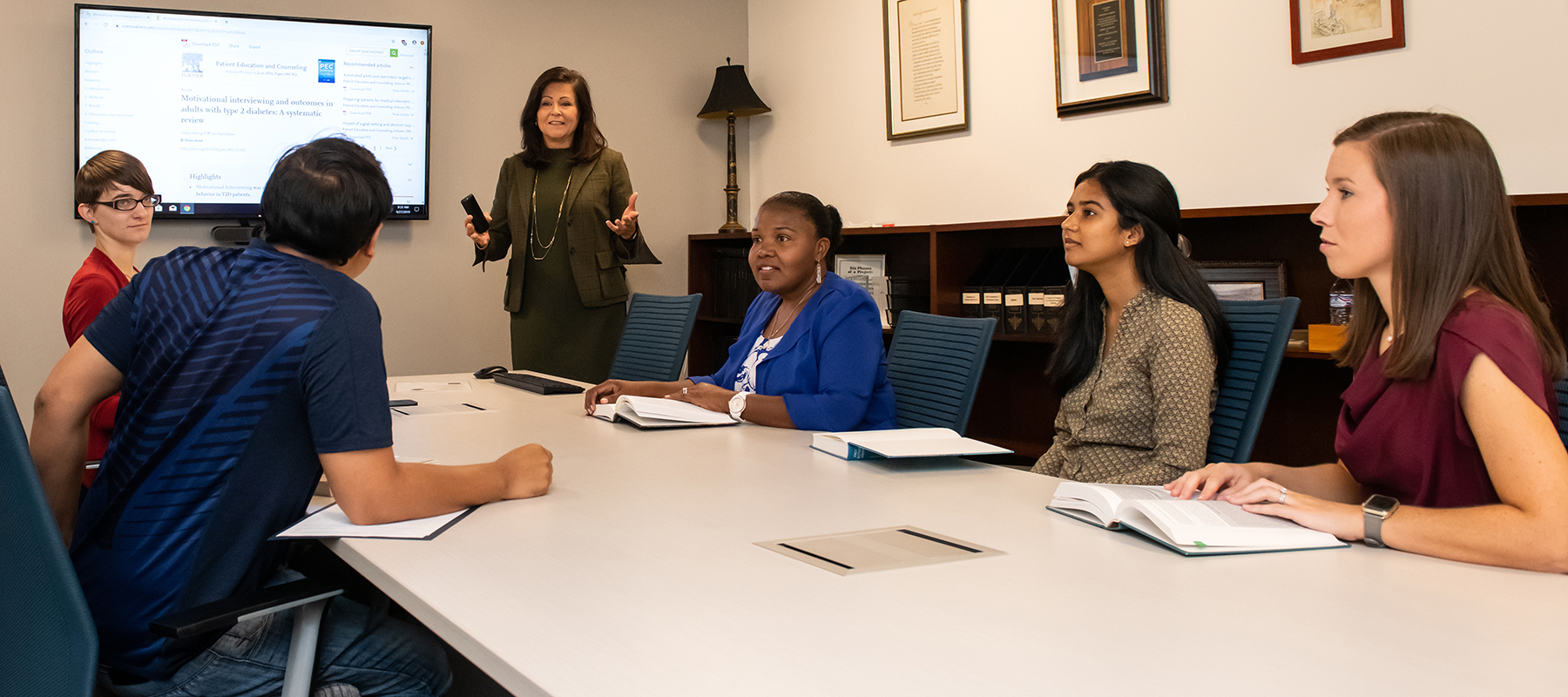 Group of students listen to instructor while sitting around conference table