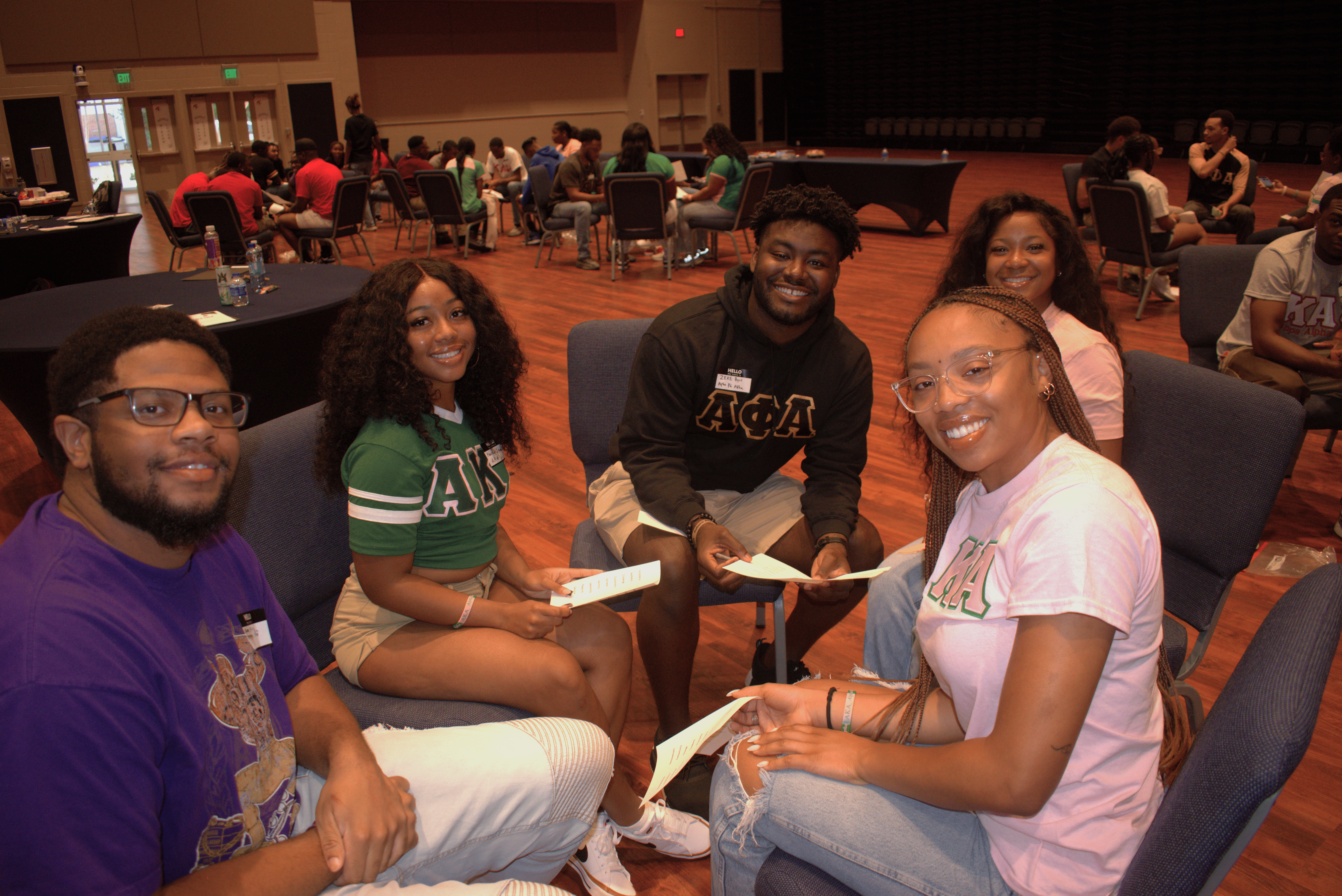 Five people sitting in a circle on chairs smiling at camera.
