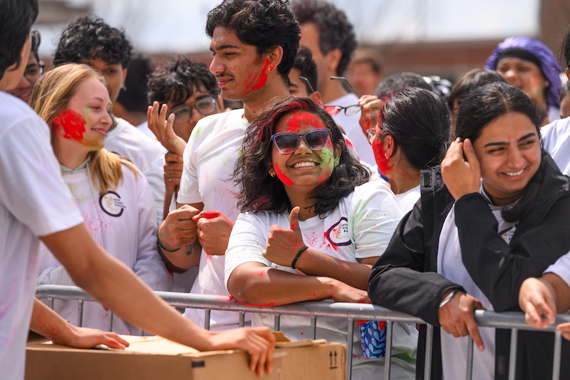 a student with paint on her face smiling and giving a thumbs up while surrounded by other students