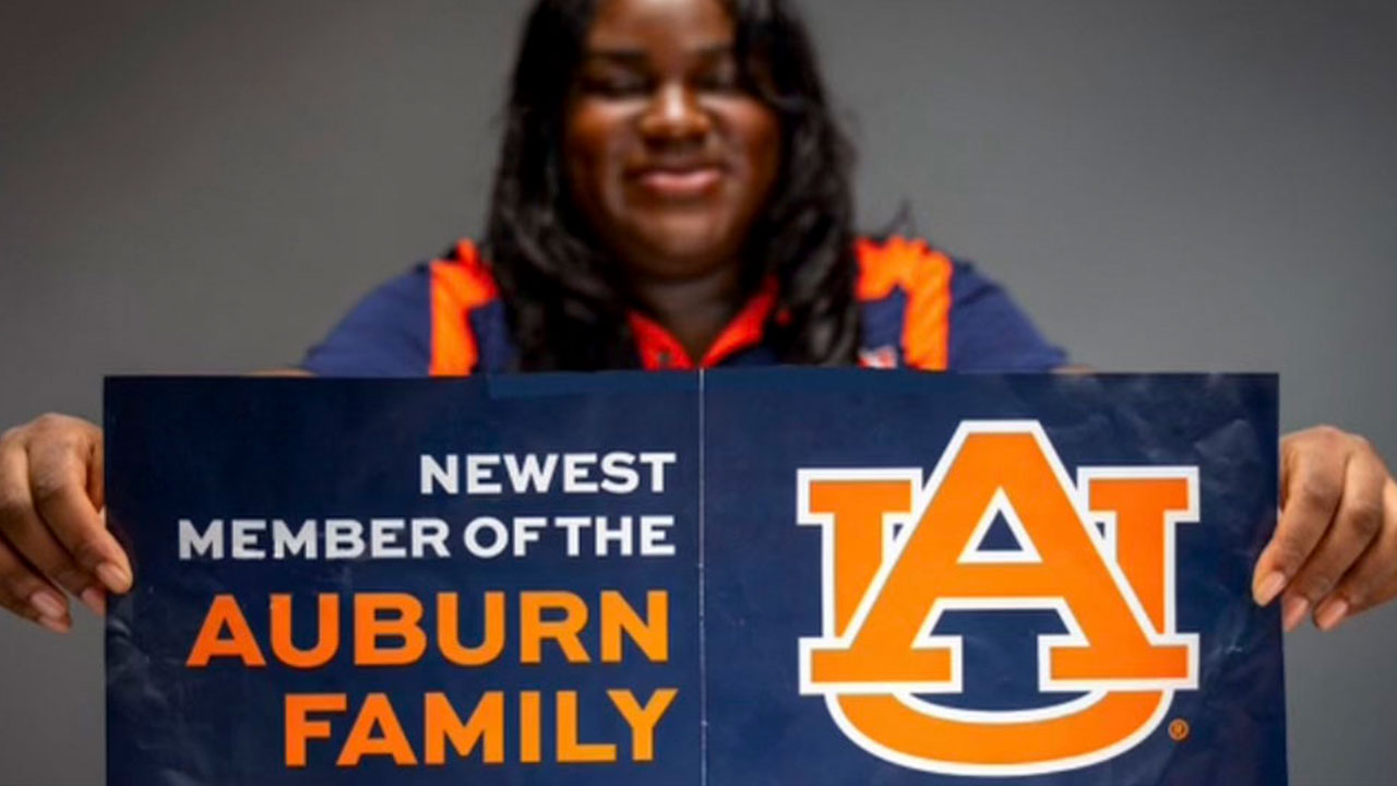 Student holding a flyer with the interlocking AU logo that says Newest Member of the Auburn Family